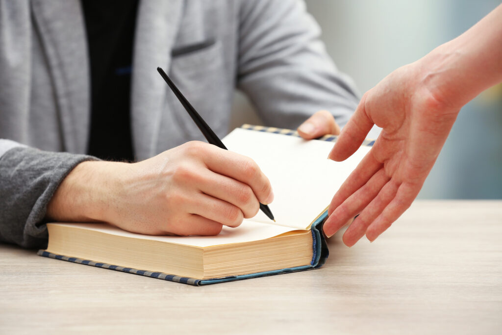 Author signing autograph in own book at wooden table on light bl